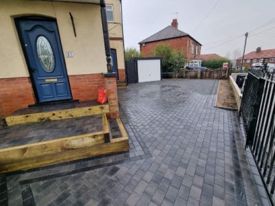 A house with a blue door and a newly paved driveway with grey brickwork. A wooden retaining wall lines the edge of the driveway.